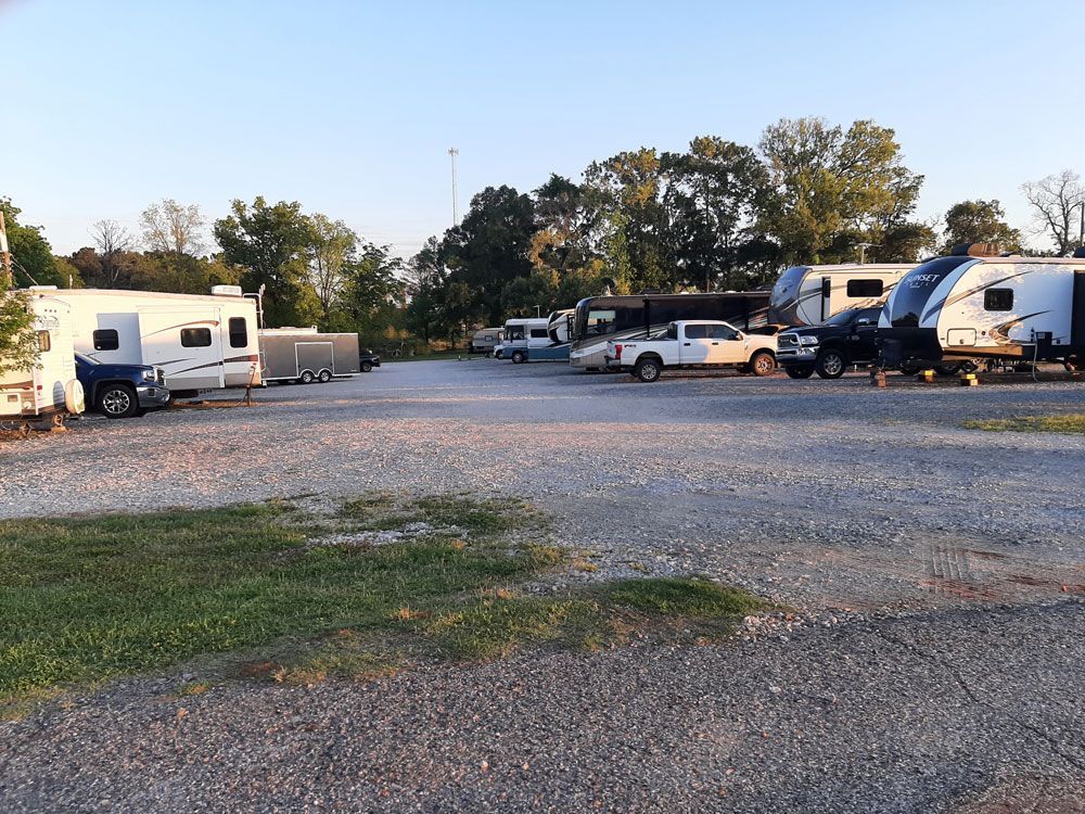 RV parking lot with several trailers and trucks on gravel.