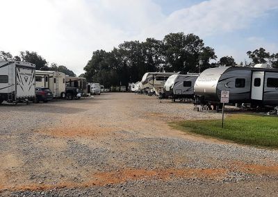 RV park with gravel drive and parked trailers on either side, under a cloudy sky.