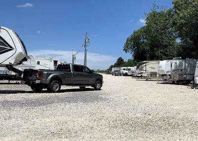 A gray pickup truck drives through a gravel lot with RVs parked on a sunny day.