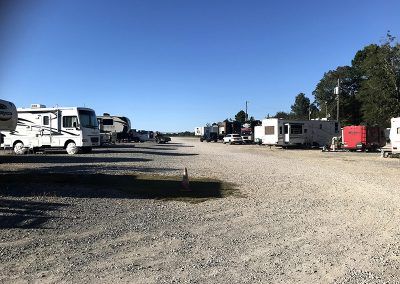 RV park with parked RVs on gravel under a blue sky.