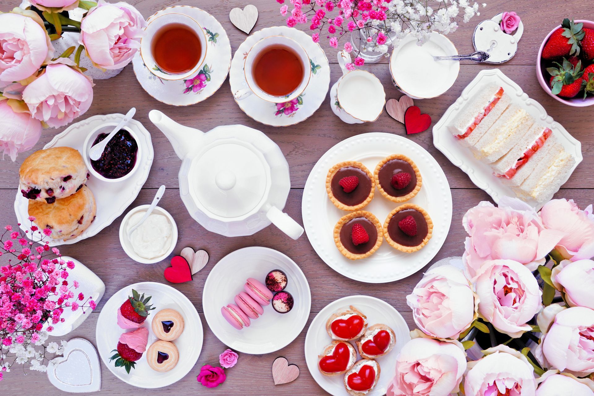 Pastel tea party spread with teapot, cups, pastries, and flowers on a pink tablecloth