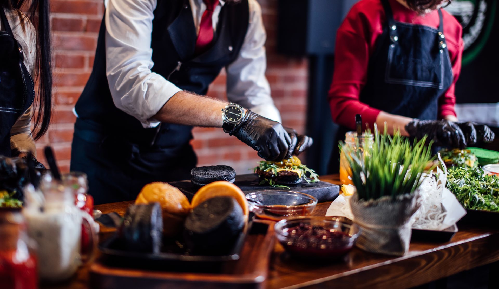 People in aprons preparing food at a table with vegetables, bowls, and kitchen tools