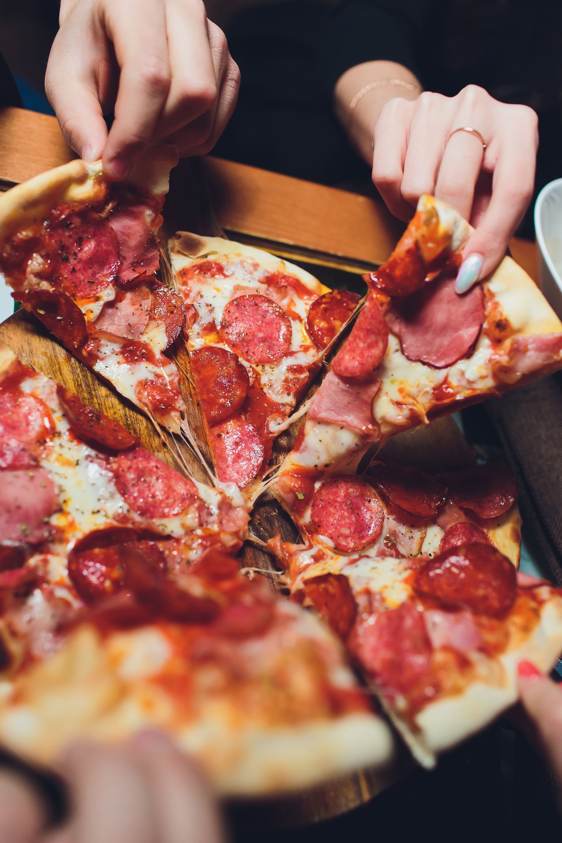 Hands lifting pepperoni pizza slices from a box