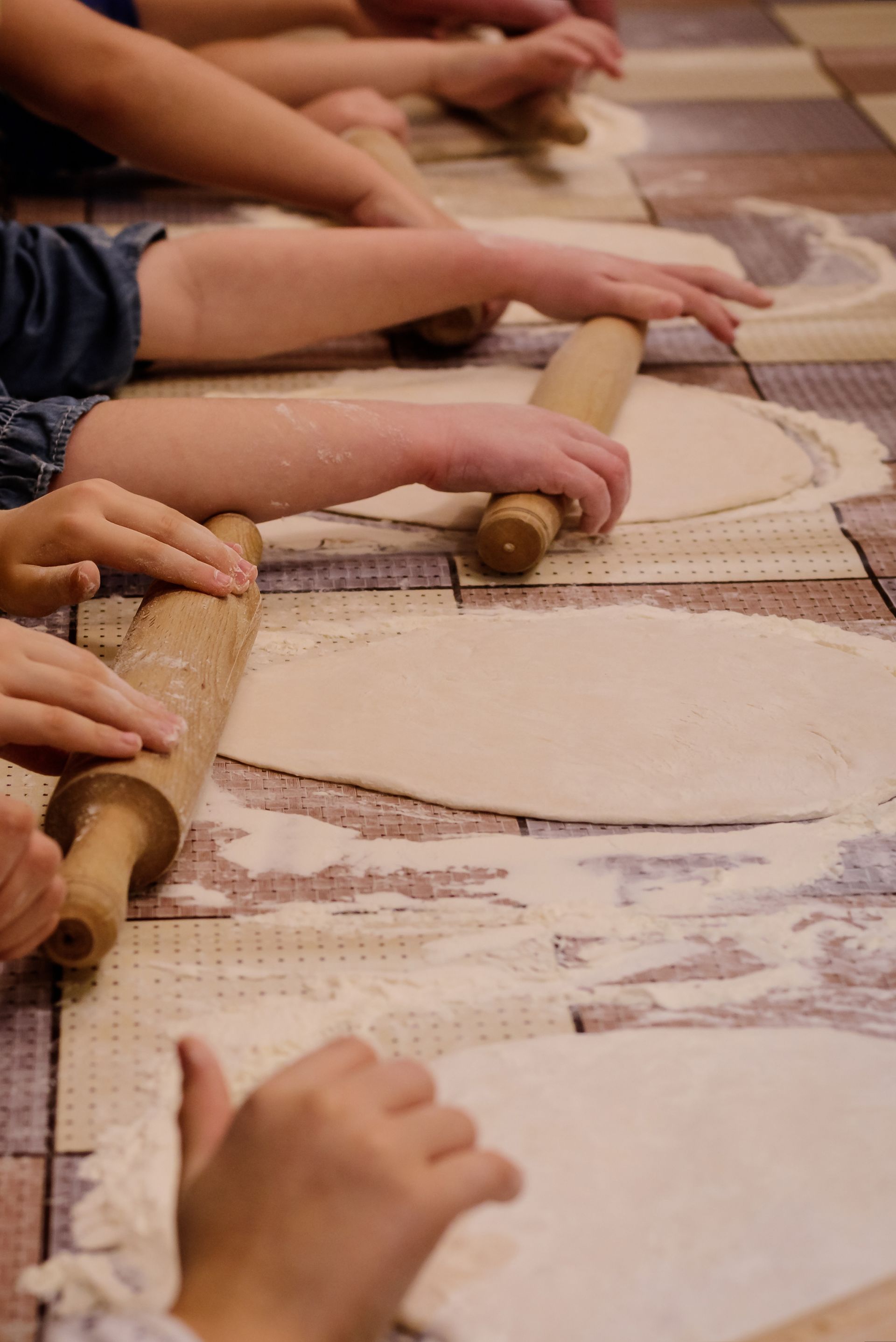Hands rolling dough with wooden rolling pins on a flour-dusted table