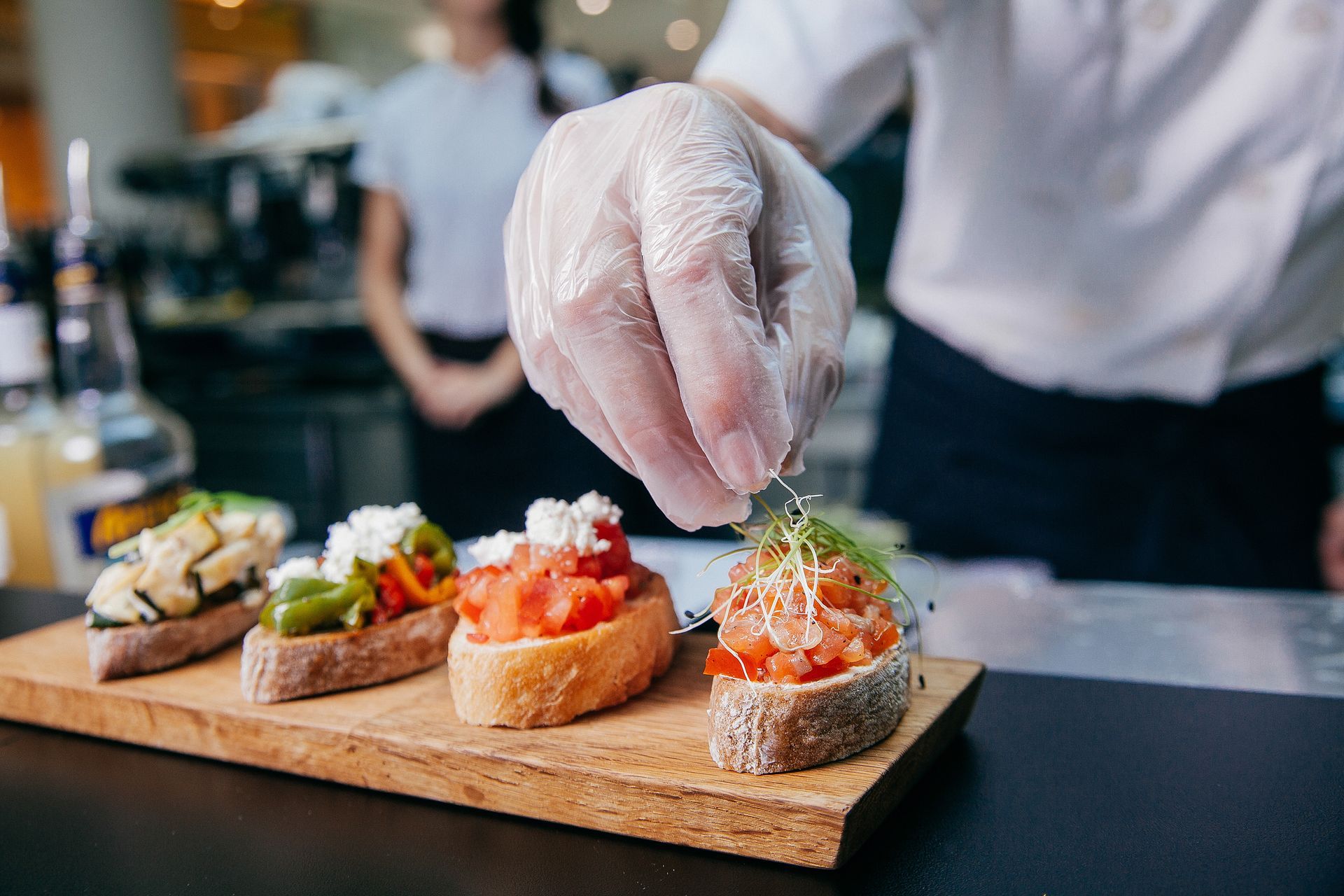 Chef garnishing assorted appetizers on a wooden board at a restaurant counter