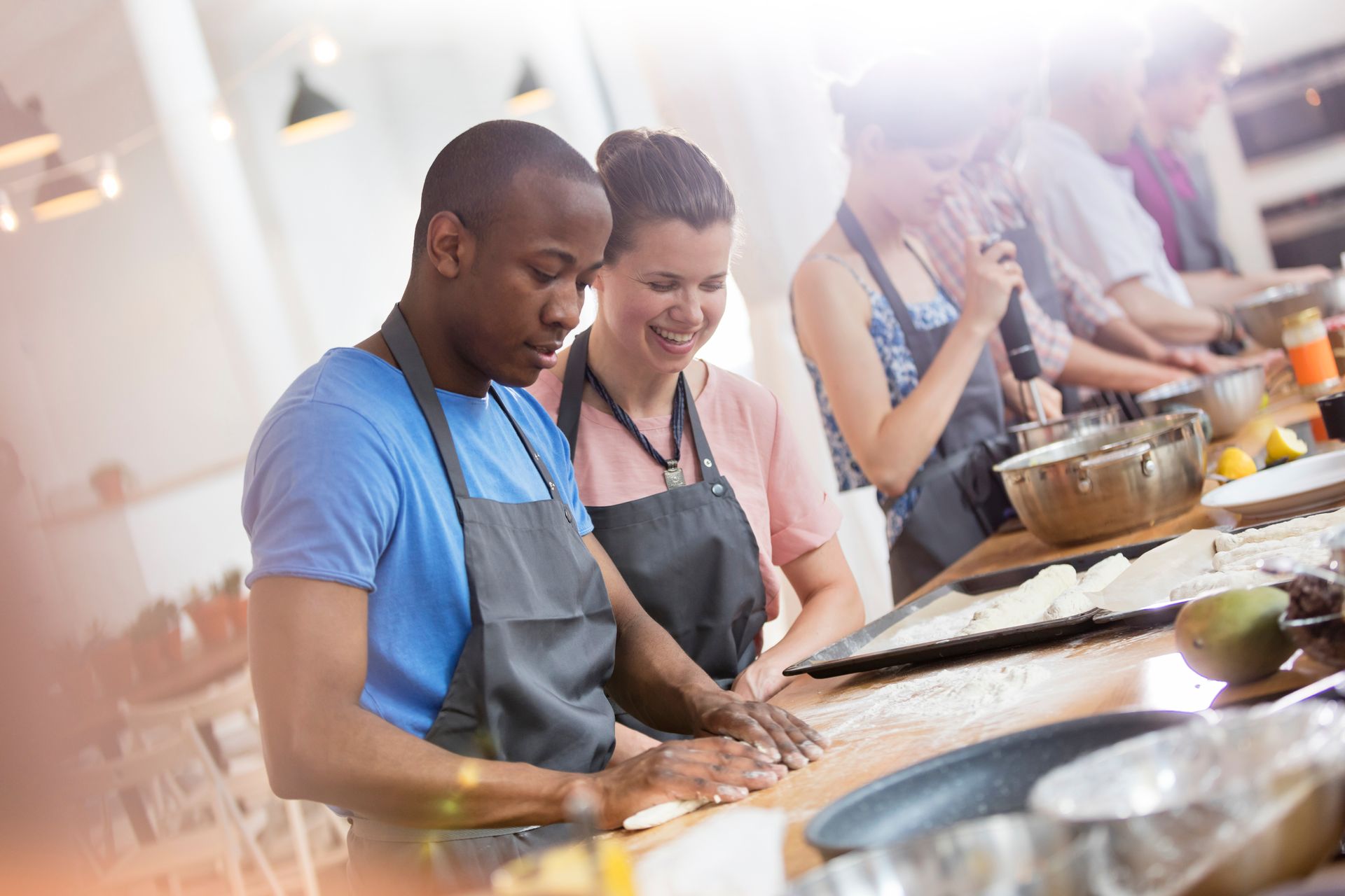 People cooking together in a bright kitchen, preparing food at a long counter.