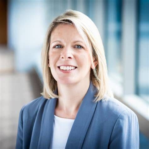 Smiling woman in a blue blazer standing in a bright office setting.