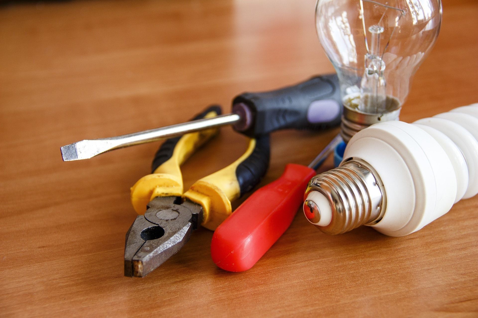 a pair of pliers, a screwdriver, and a light bulb are on a wooden table
