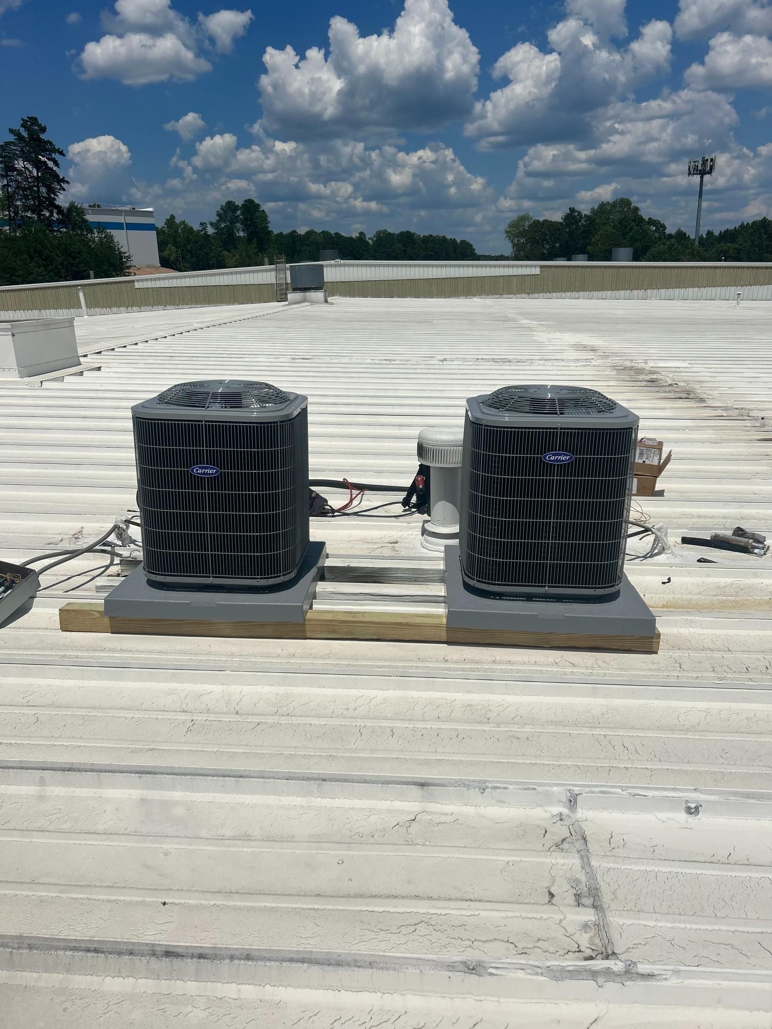 Two rooftop HVAC units on a white roof under a partly cloudy blue sky.