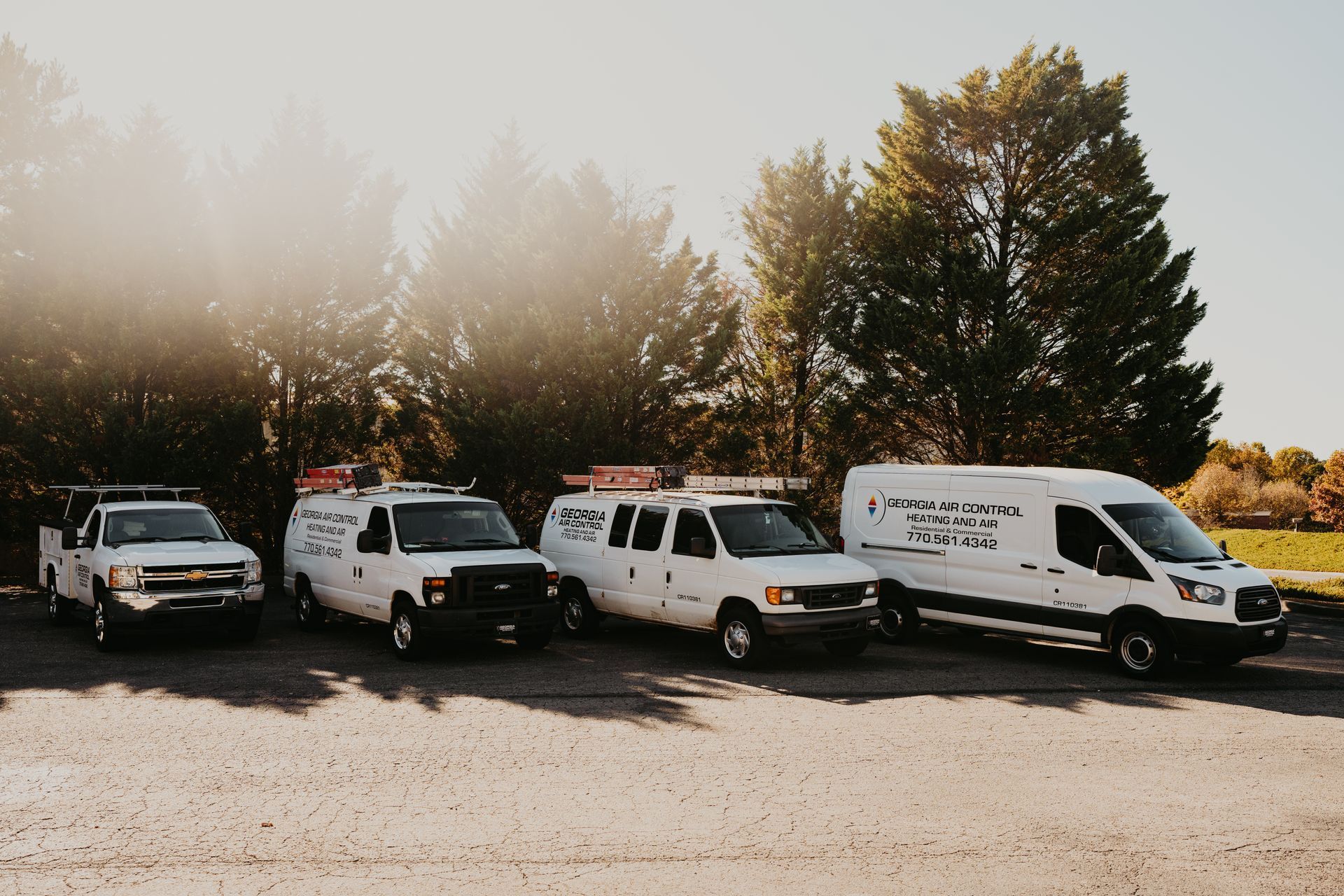 A row of white vans are parked in a gravel lot