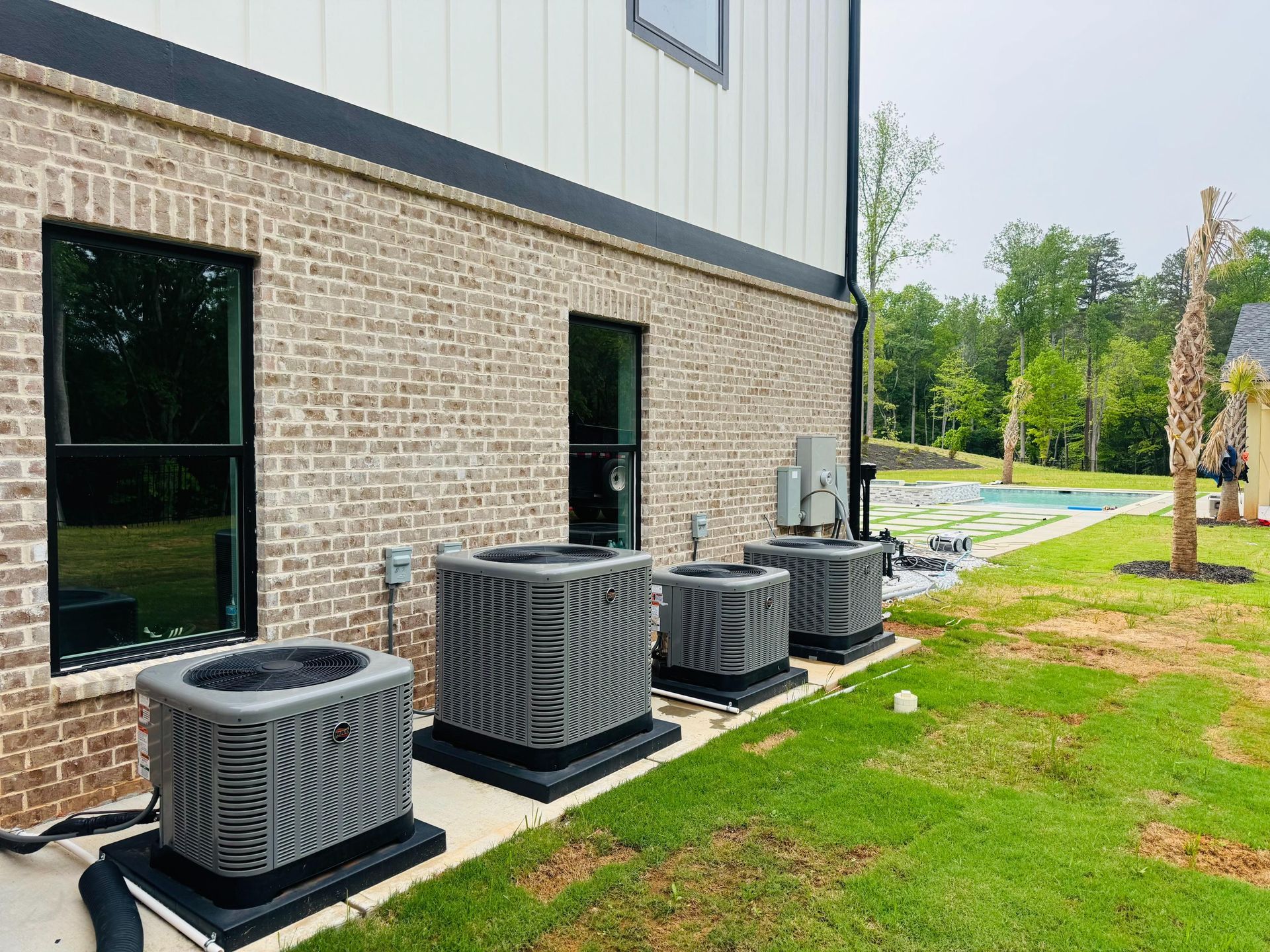Four outdoor HVAC units beside a brick building on a grassy lawn