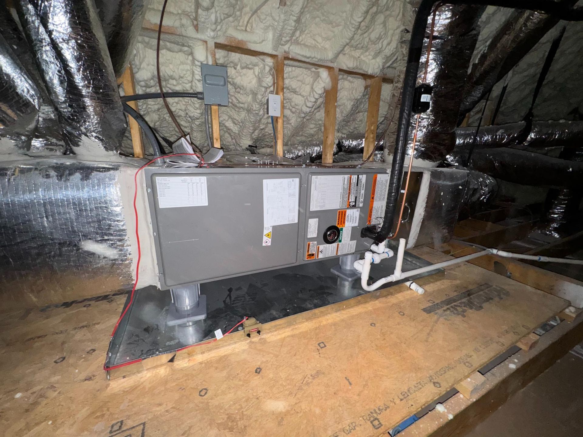 Gray HVAC unit installed in an attic with insulated walls and exposed ductwork.