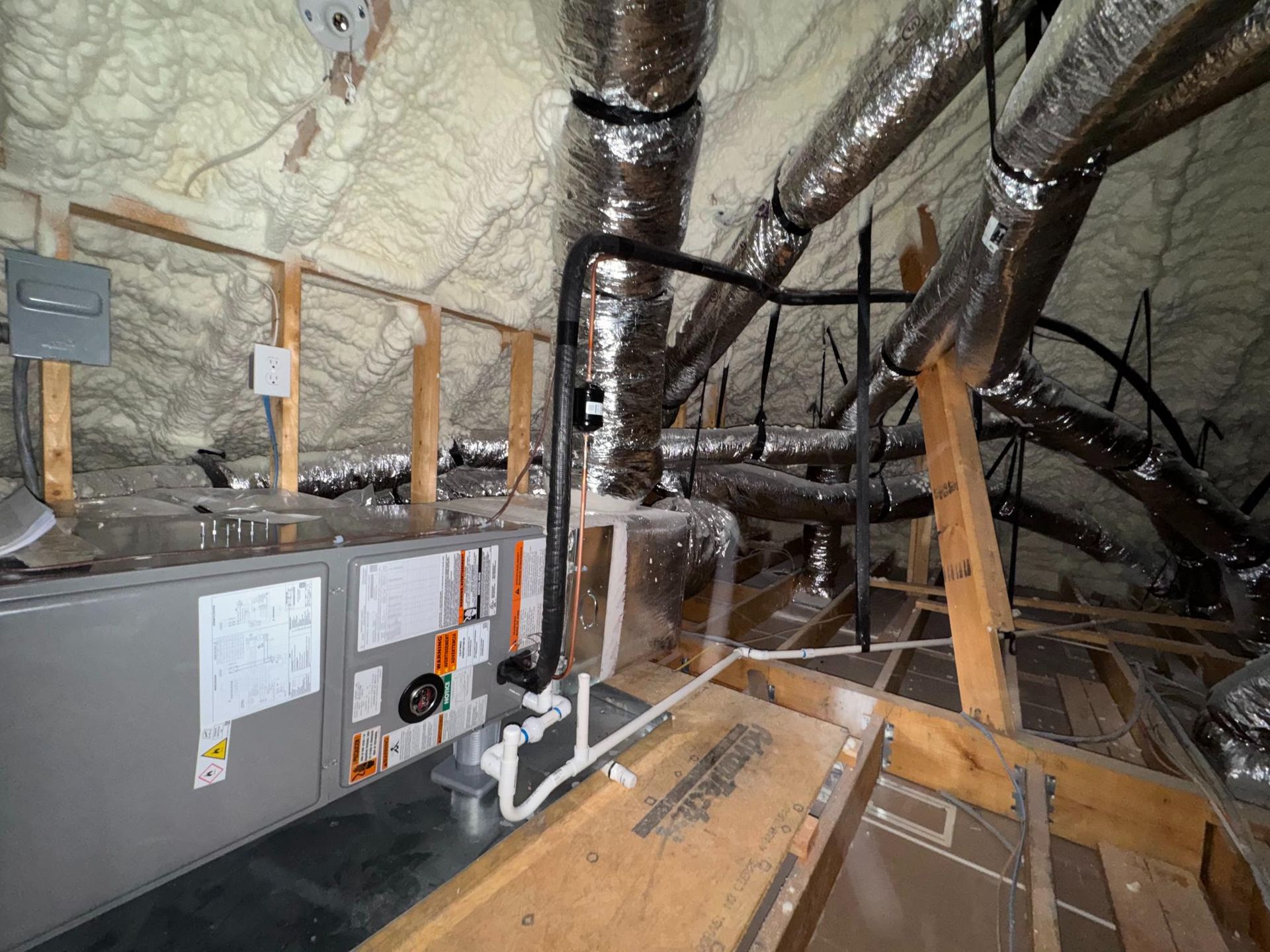 Attic with HVAC ducts, insulation, and a gray utility unit amid exposed wooden framing