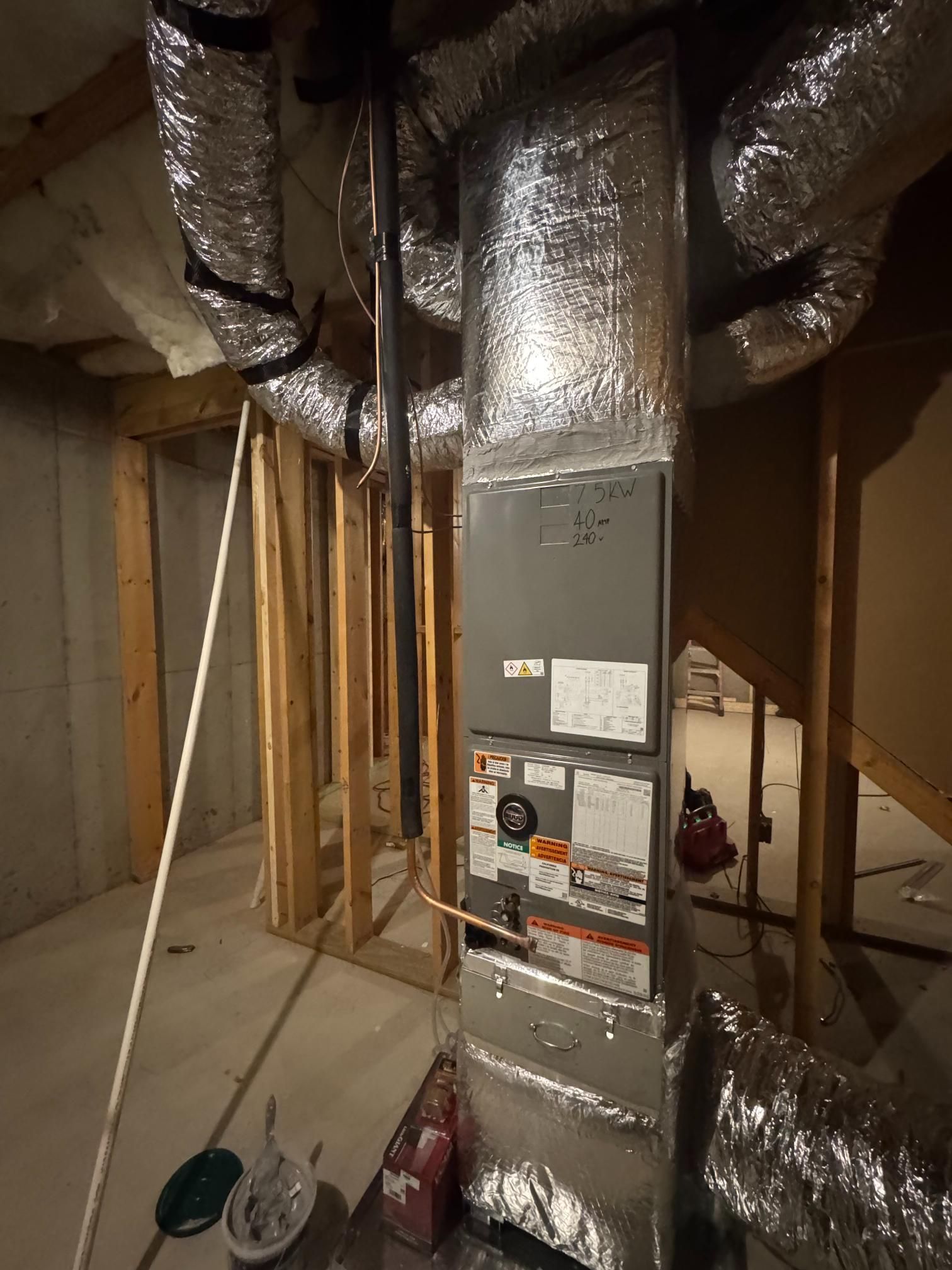 Unfinished basement with a metal HVAC furnace, exposed ductwork, and framed walls in a construction area