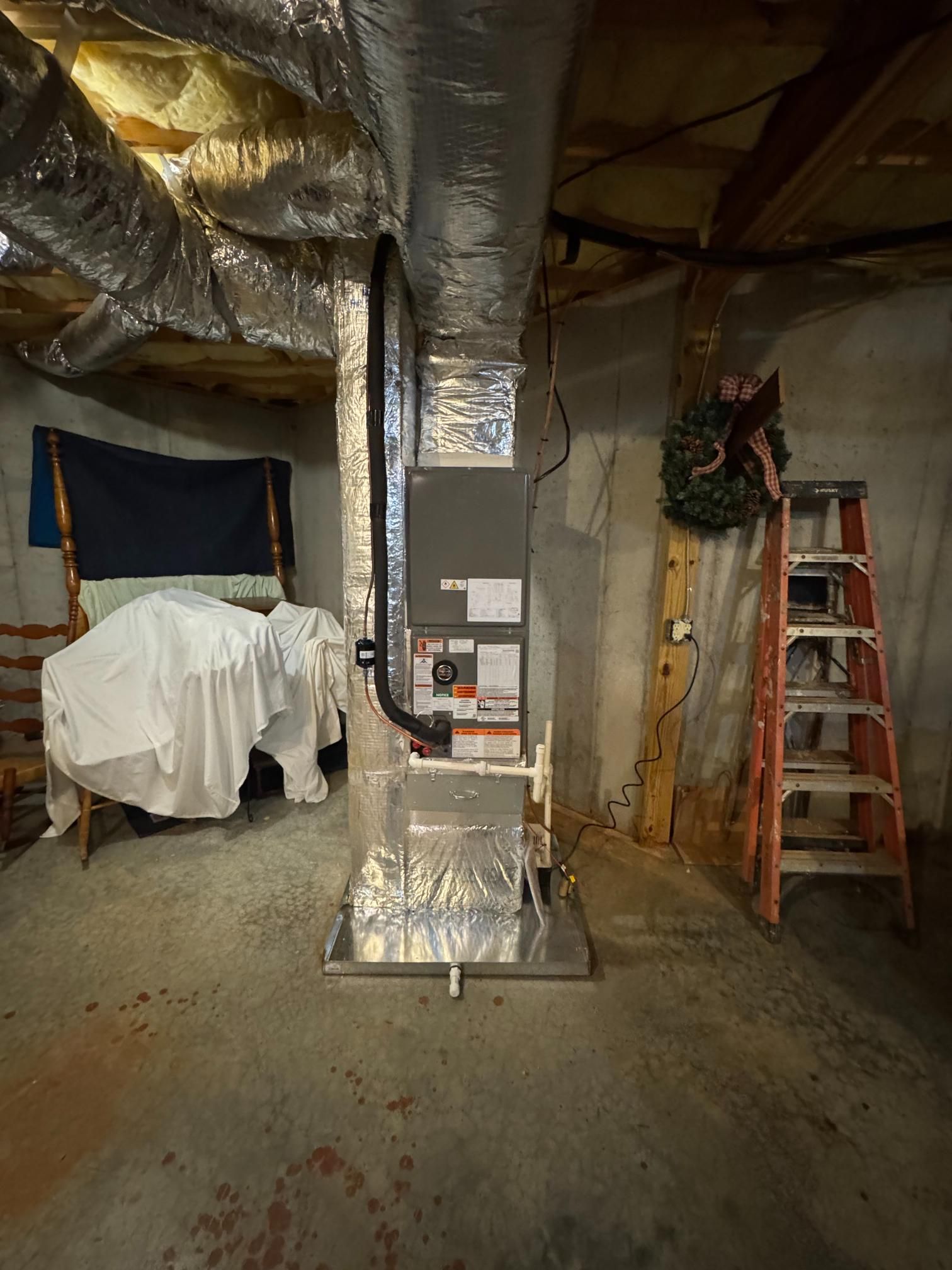 Basement with HVAC ductwork, insulated pipes, a covered object, and a ladder beside a decorated post