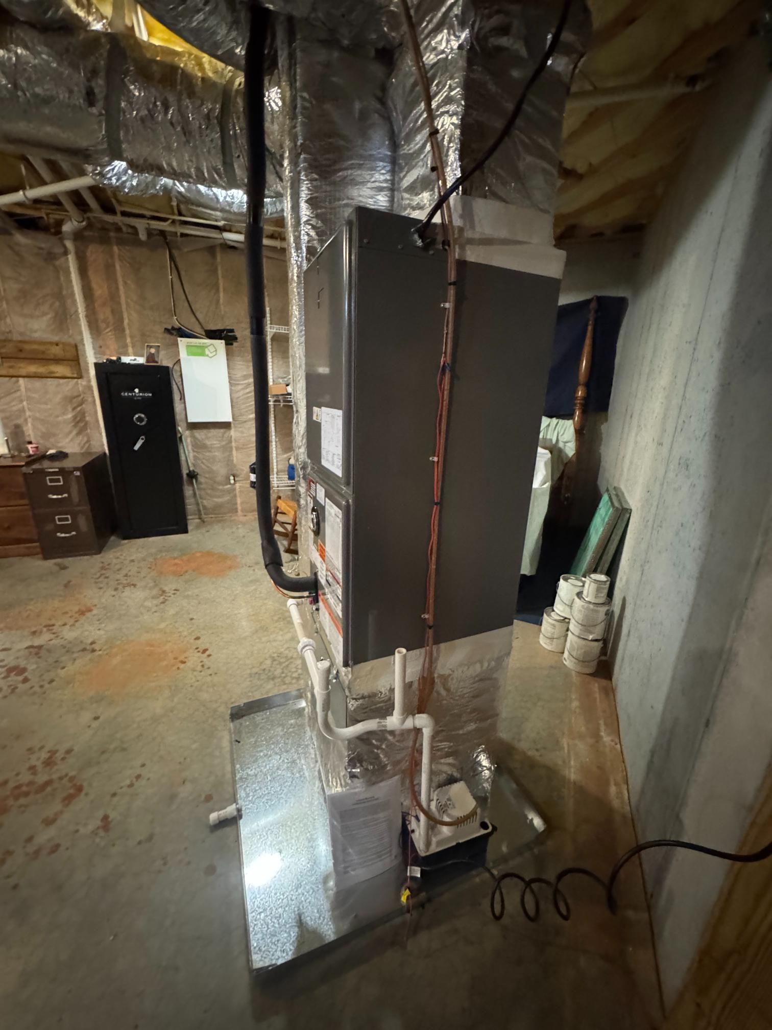 Basement utility room with HVAC ducts, metal furnace, and exposed insulation.