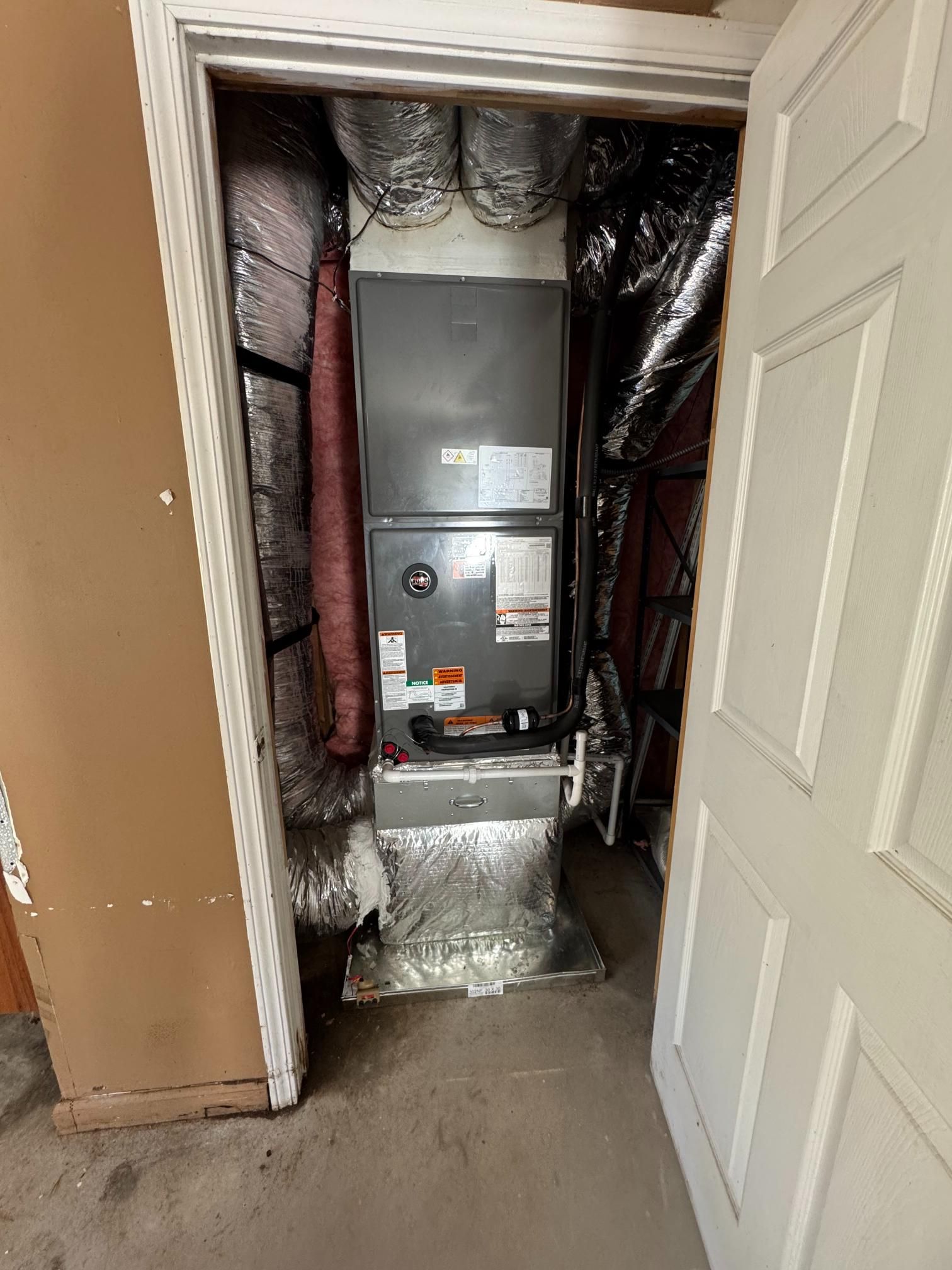Open closet reveals HVAC unit and insulated ductwork in a narrow utility space.