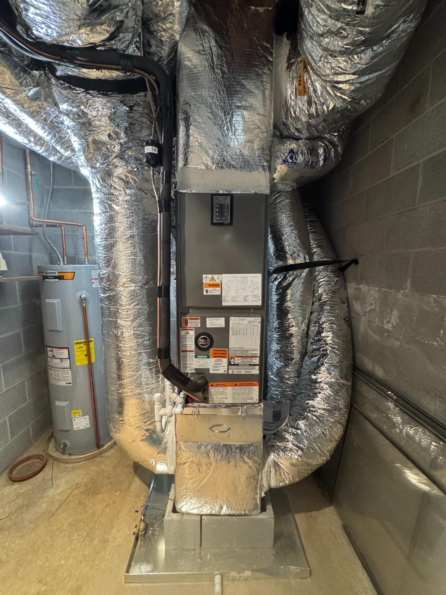 Central HVAC furnace in a utility room, surrounded by insulated ductwork and water heater tanks