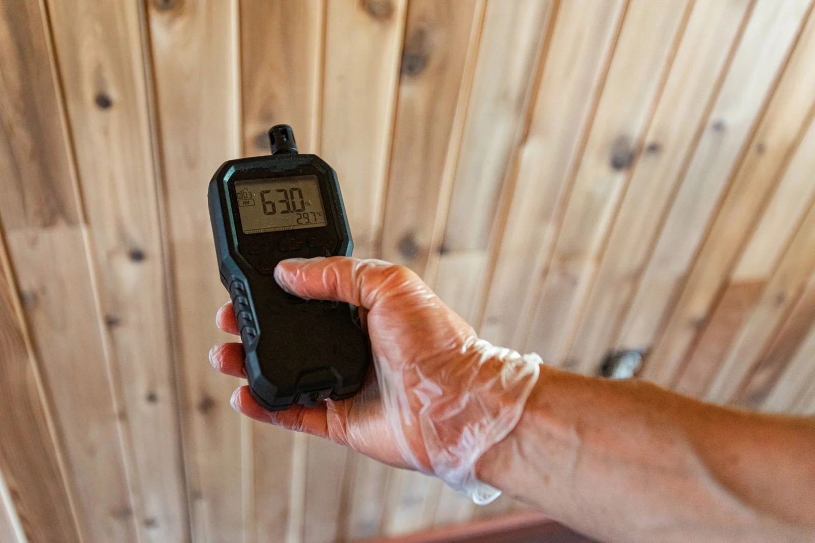 Hand holding a digital moisture meter against a wooden wall