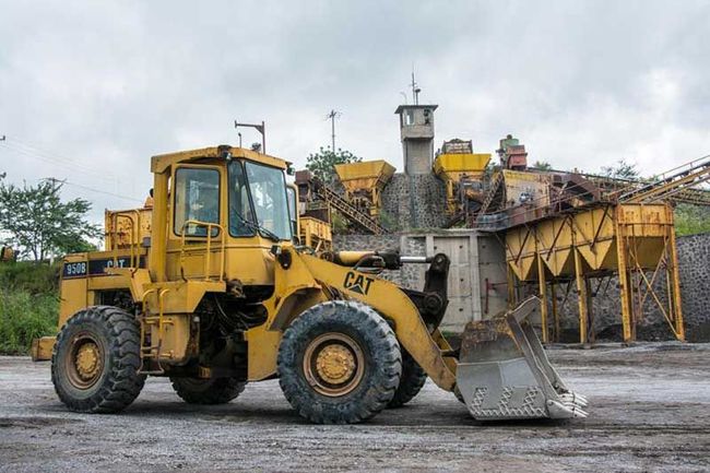 Una excavadora amarilla está estacionada frente a un montón de rocas.