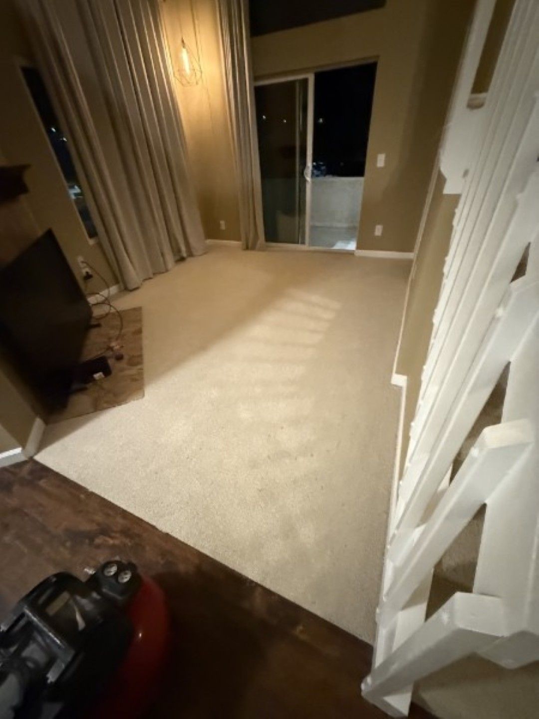 Empty carpeted living room with sliding glass doors and curtains at night