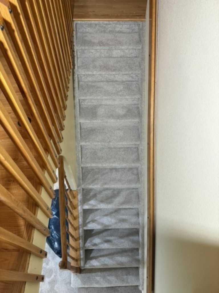 Staircase with a narrow gray carpet runner between wooden railings and a cream wall.