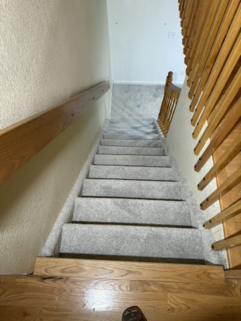 Indoor staircase with white carpeted steps, wood handrails, and light walls, viewed from the top.