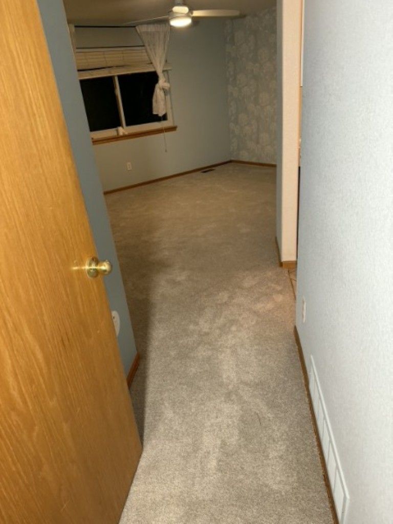Empty carpeted room with open wood door, window, and ceiling fan.