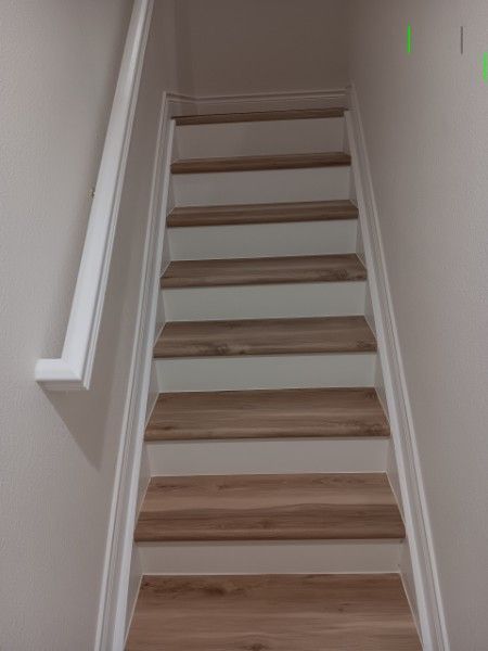Narrow indoor staircase with white walls, handrail, and wood steps