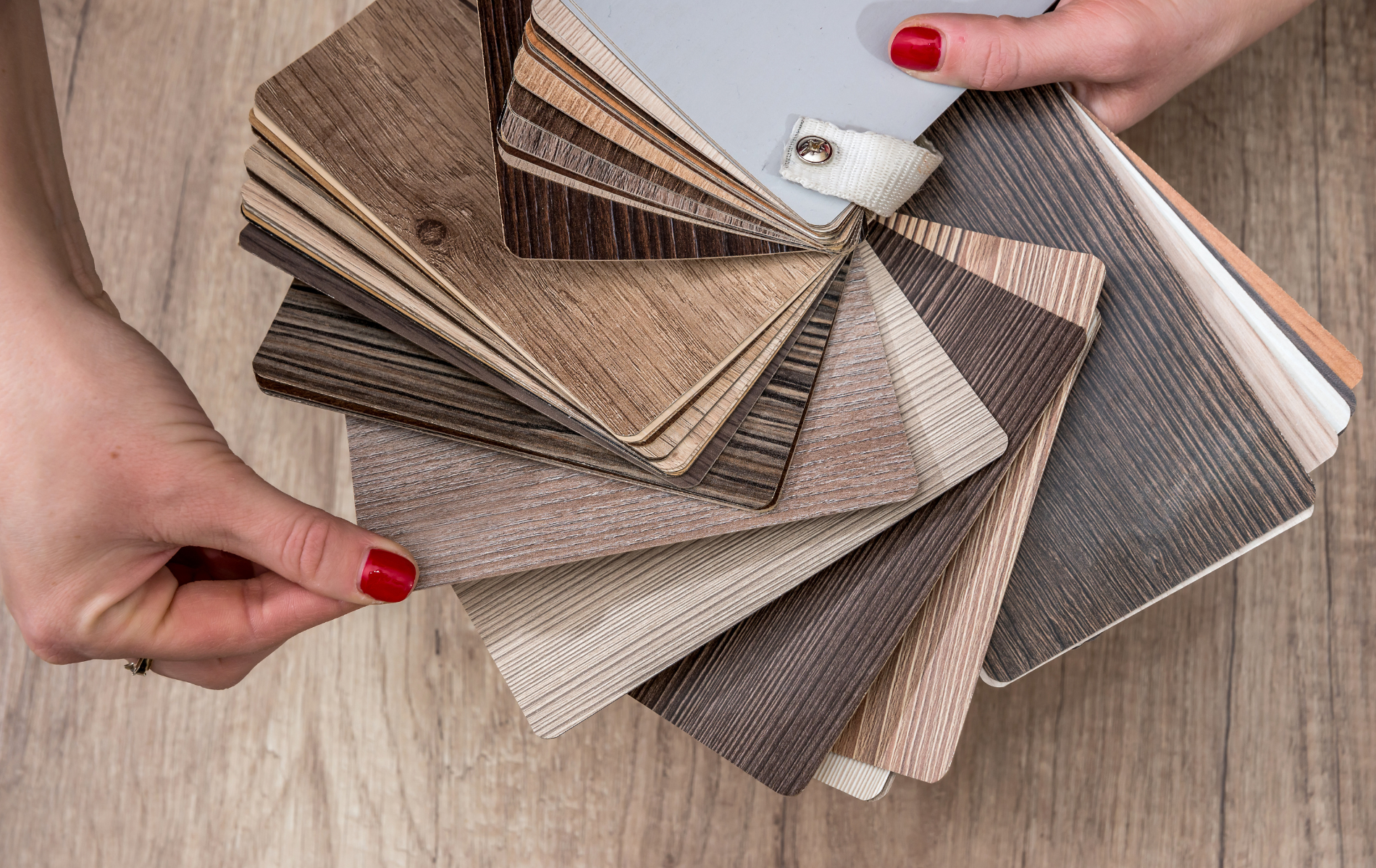Hands holding a fan of neutral-toned fabric swatches over a wooden surface