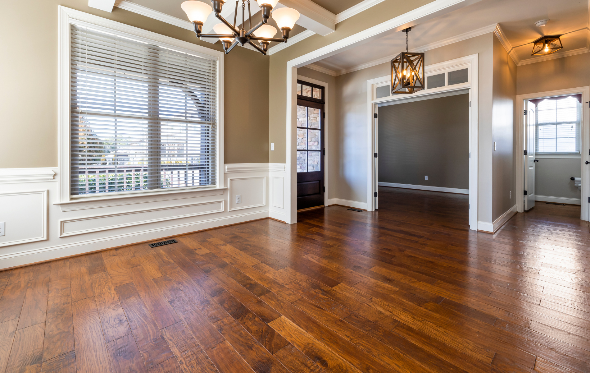 Bright empty dining room with hardwood floors, white wainscoting, and large window blinds