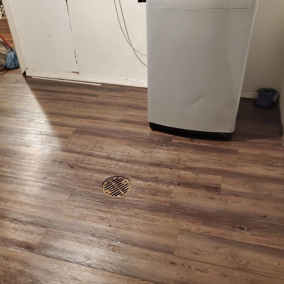 Wood-look floor with a small circular drain, a white cabinet, and a black bowl in the corner.