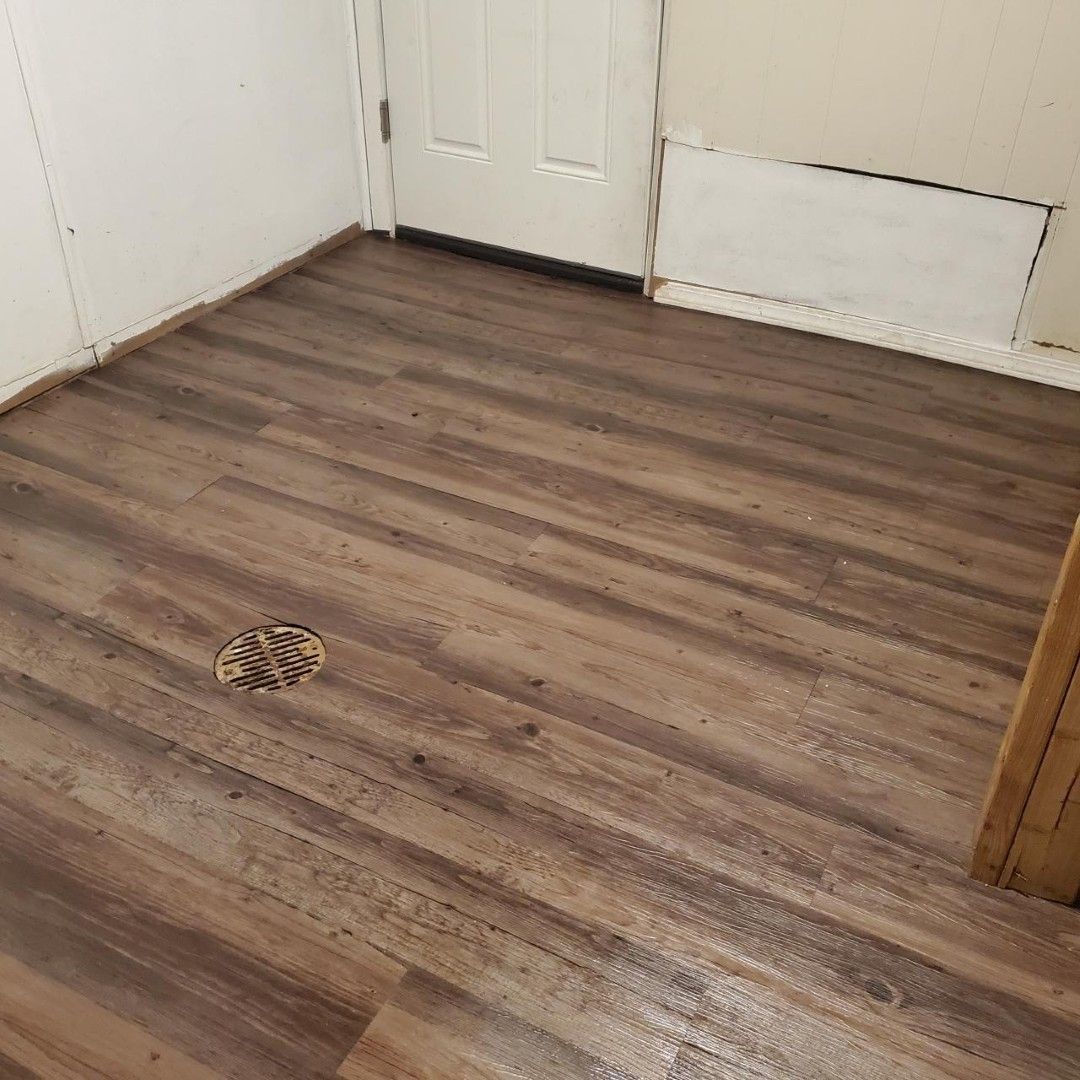 Empty room with wood-look flooring, white walls, and a floor drain near the center.