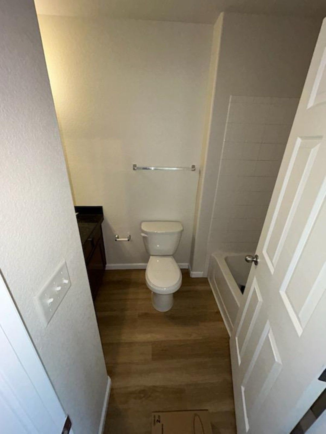 Small bathroom with a toilet, wood-look floor, towel bar, and shower tub on the right.