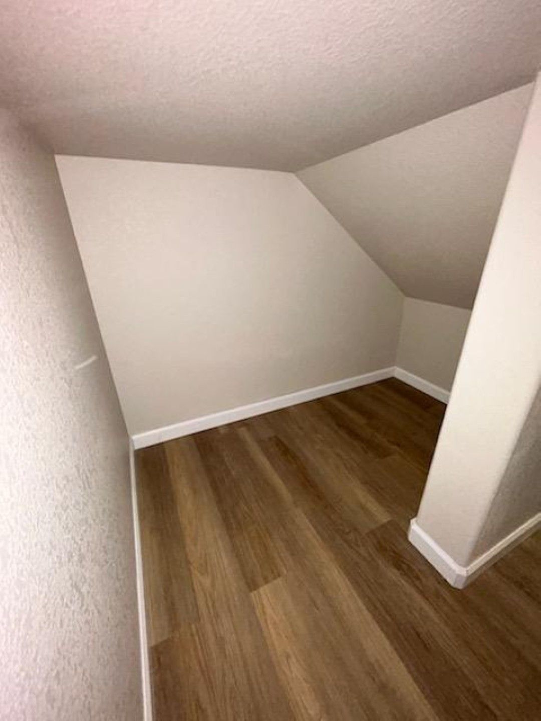 Small slanted attic nook with white walls and wood flooring, viewed from the doorway.
