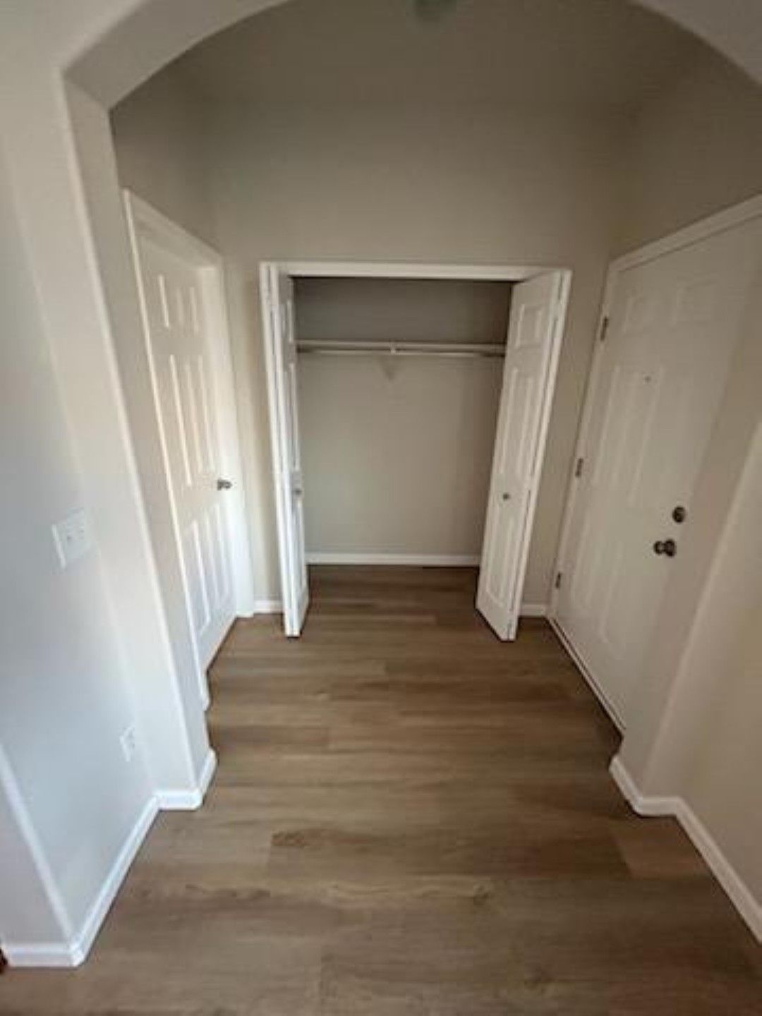 Empty hallway with a closet, white walls, and wood flooring