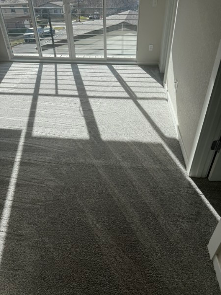 Empty carpeted room with sunlight casting grid shadows from a window and balcony door.