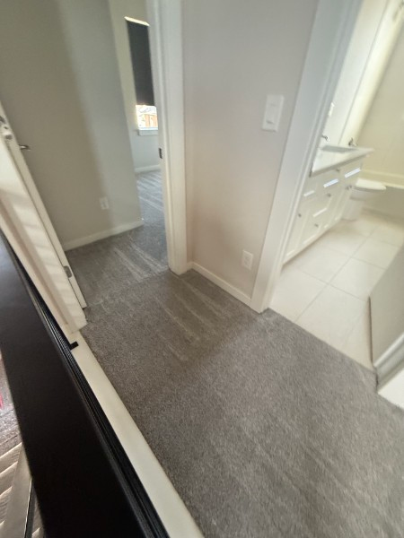 Hallway with gray carpet leading to a white bathroom with tile floor and vanity.