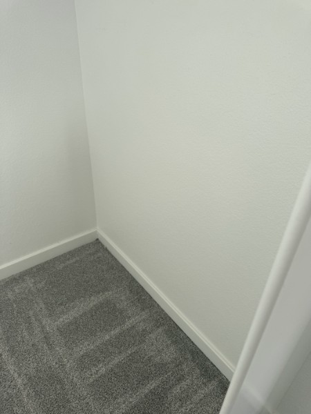 Empty carpeted corner of a room with white walls and baseboards