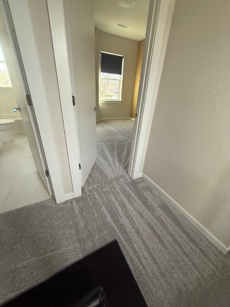 Narrow hallway with gray carpet, white walls, and a small window at the end.