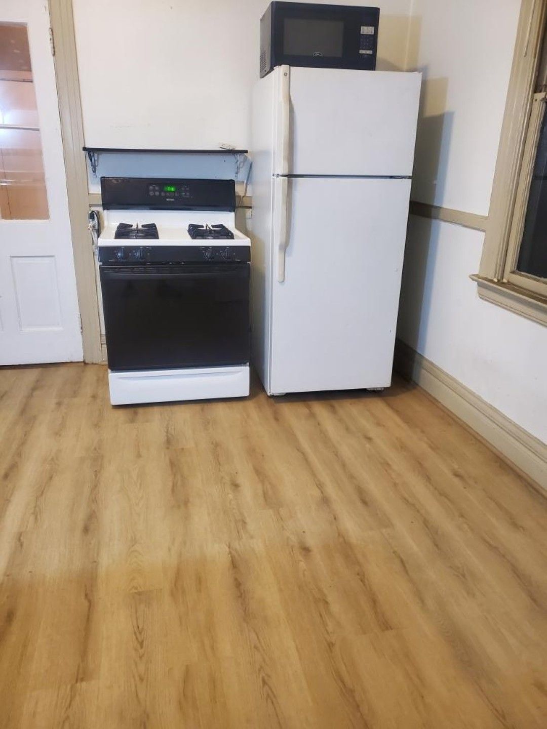 Small kitchen with white refrigerator, black stove, microwave, and wood flooring.