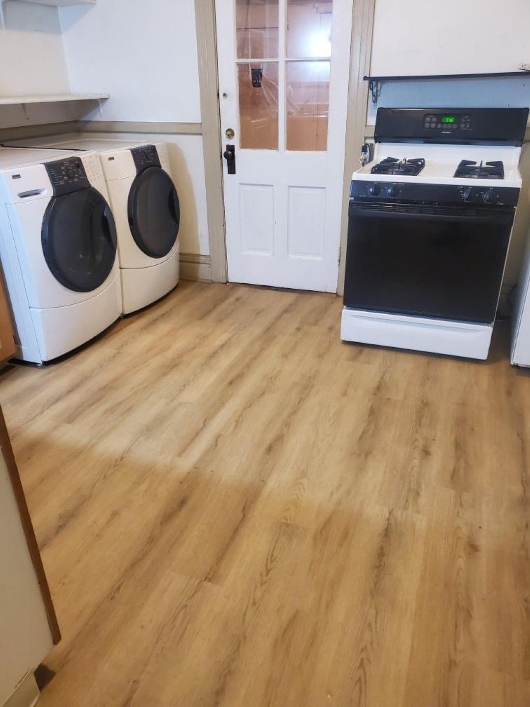 Laundry room with two front-loading washers, a white door, and a black stove on a wood floor.