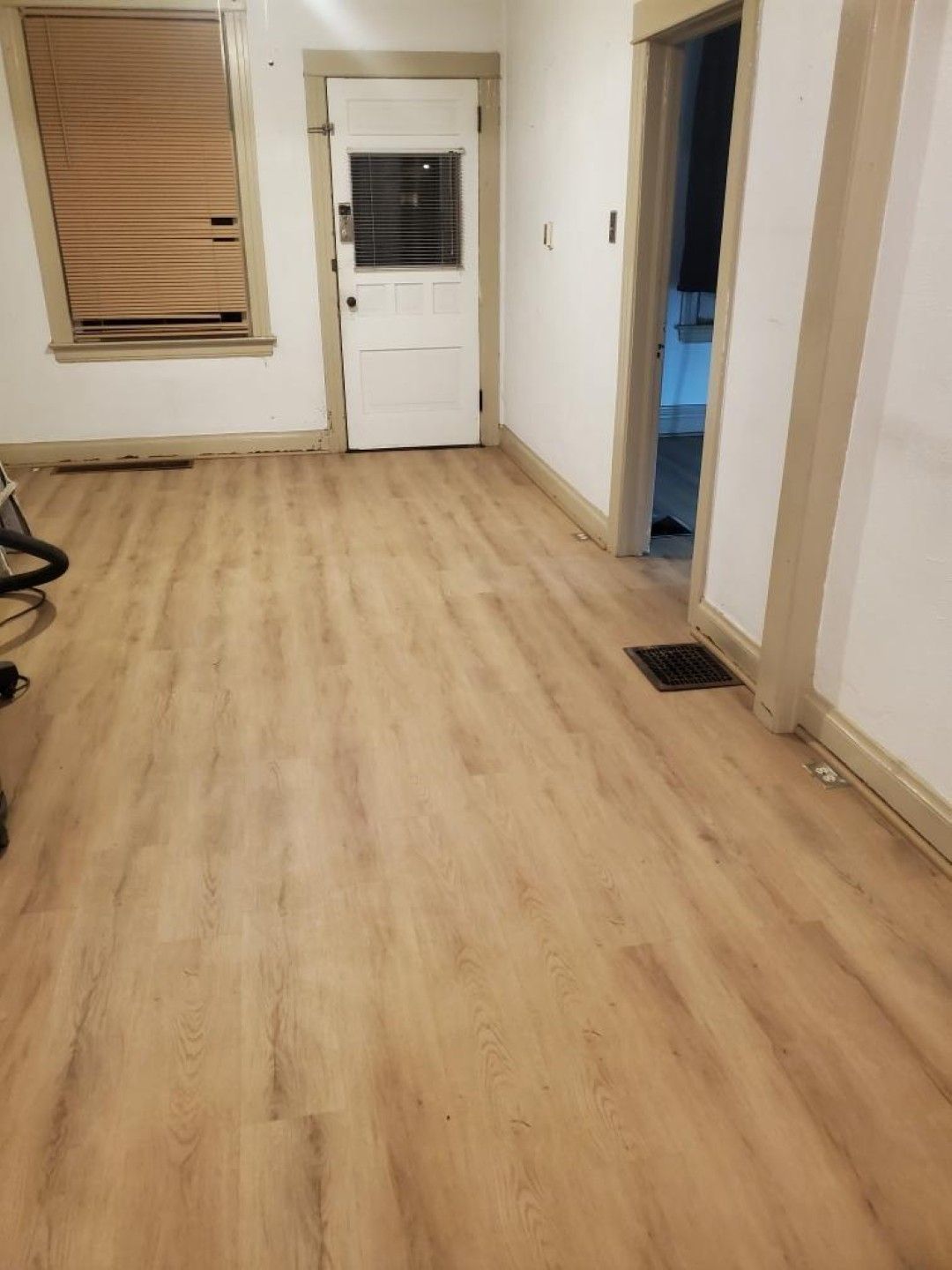 Empty room with light wood floors, a white door, and windows with blinds.