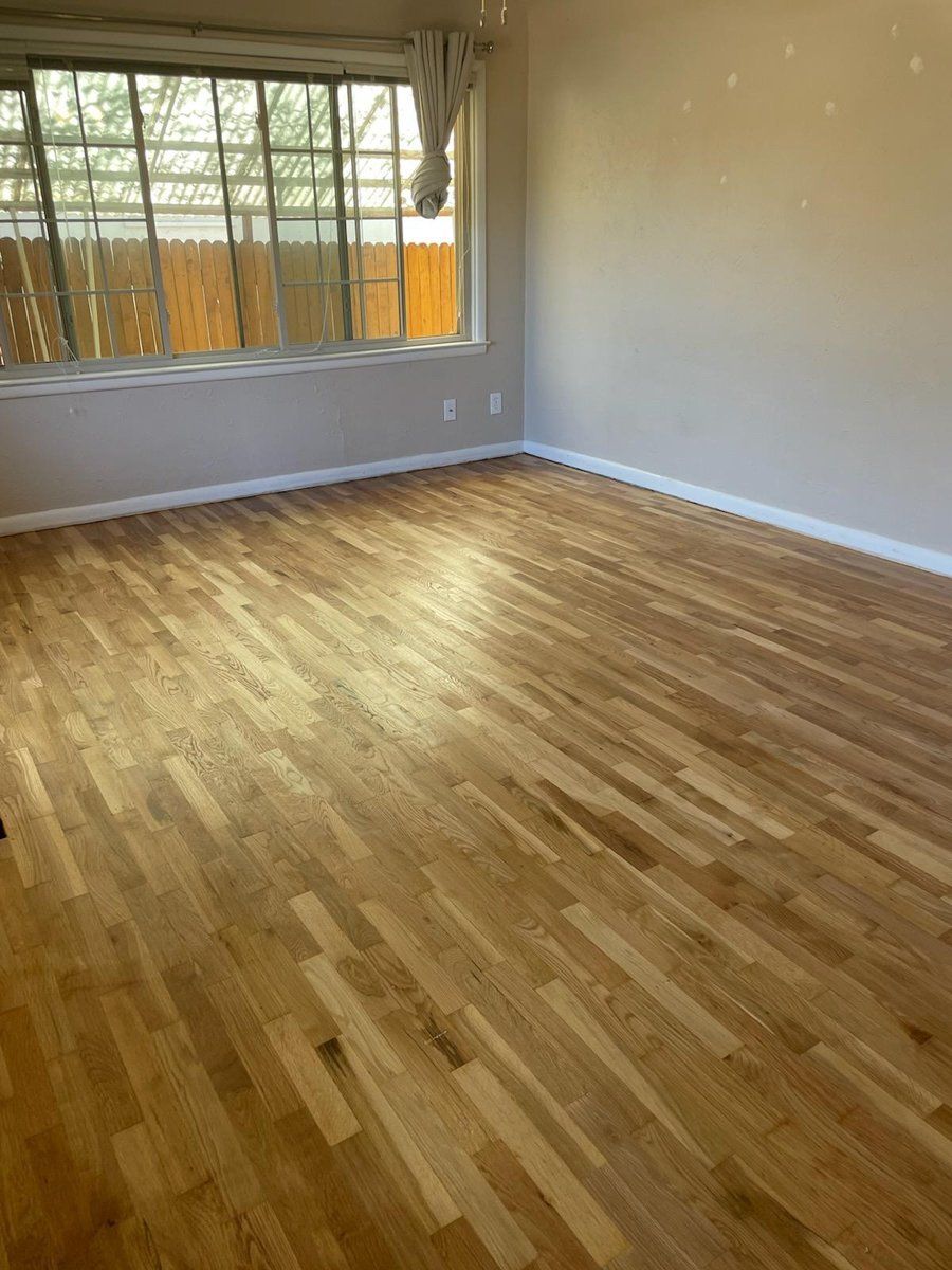 Empty room with wood flooring, gray walls, and a large window with bars.