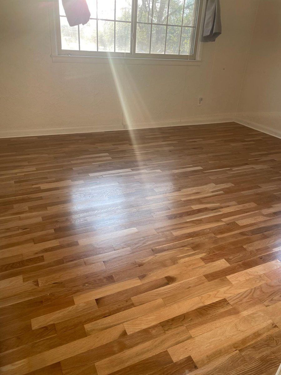 Empty room with glossy hardwood floors, white walls, and a sunlit window.