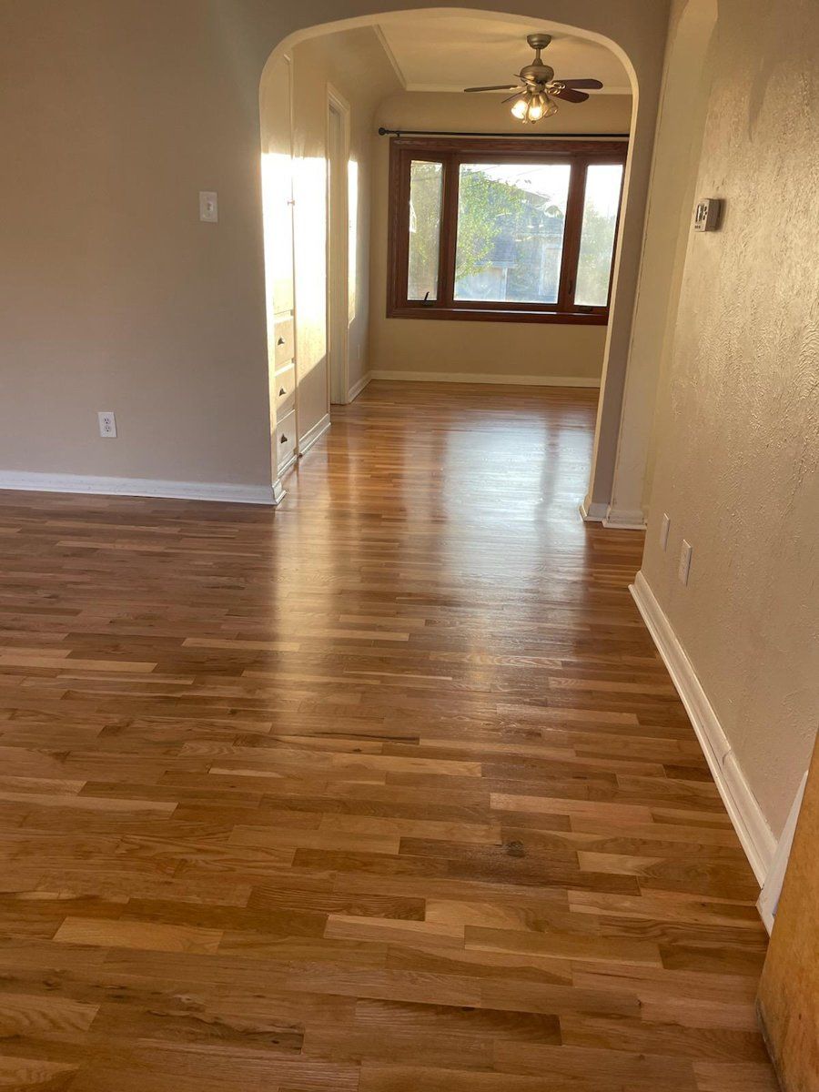 Empty room with polished hardwood floors, beige walls, and French doors to a bright outdoor view.