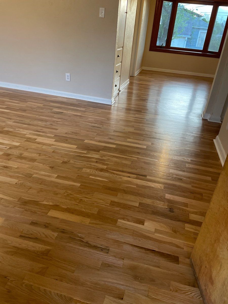 Empty hardwood-floored room with beige walls and a large window in the background