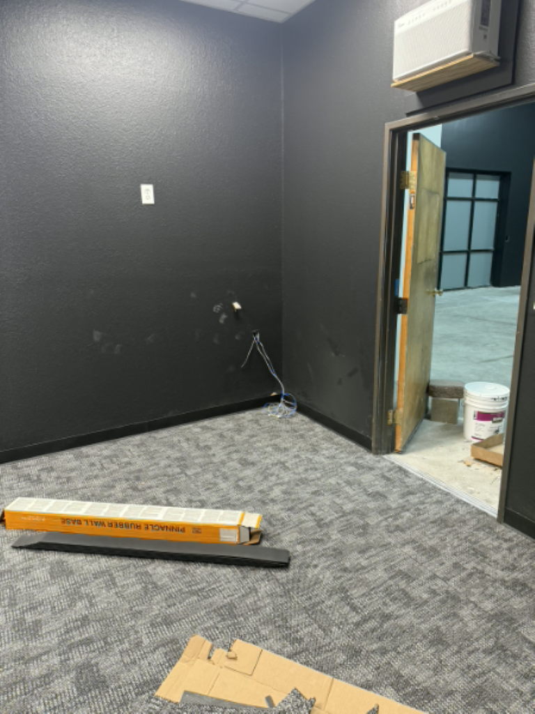 Empty dark-painted room with patterned carpet, open doorway, and construction materials on the floor.
