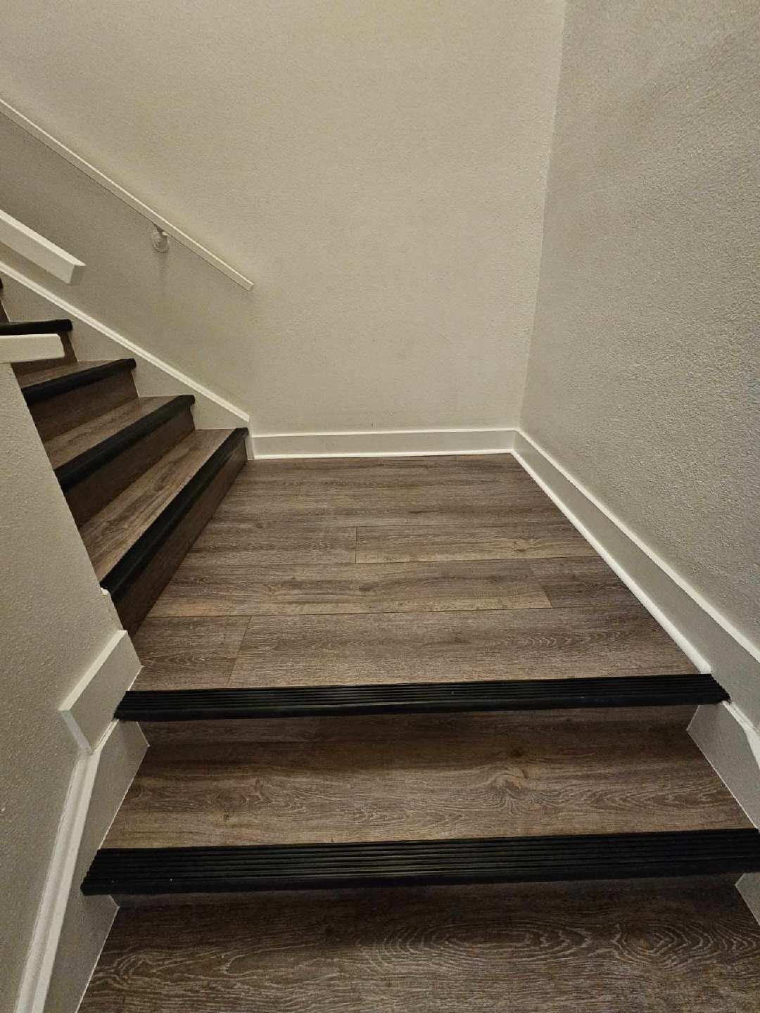 Staircase landing with wood-look flooring, beige walls, and dark-edged steps on the left.