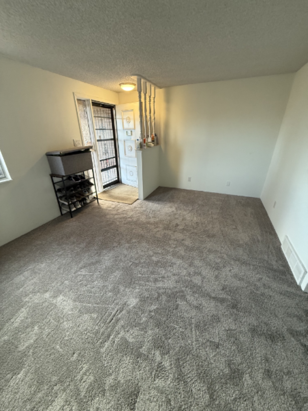 Empty carpeted room with a window, open door, and small black shelving unit.